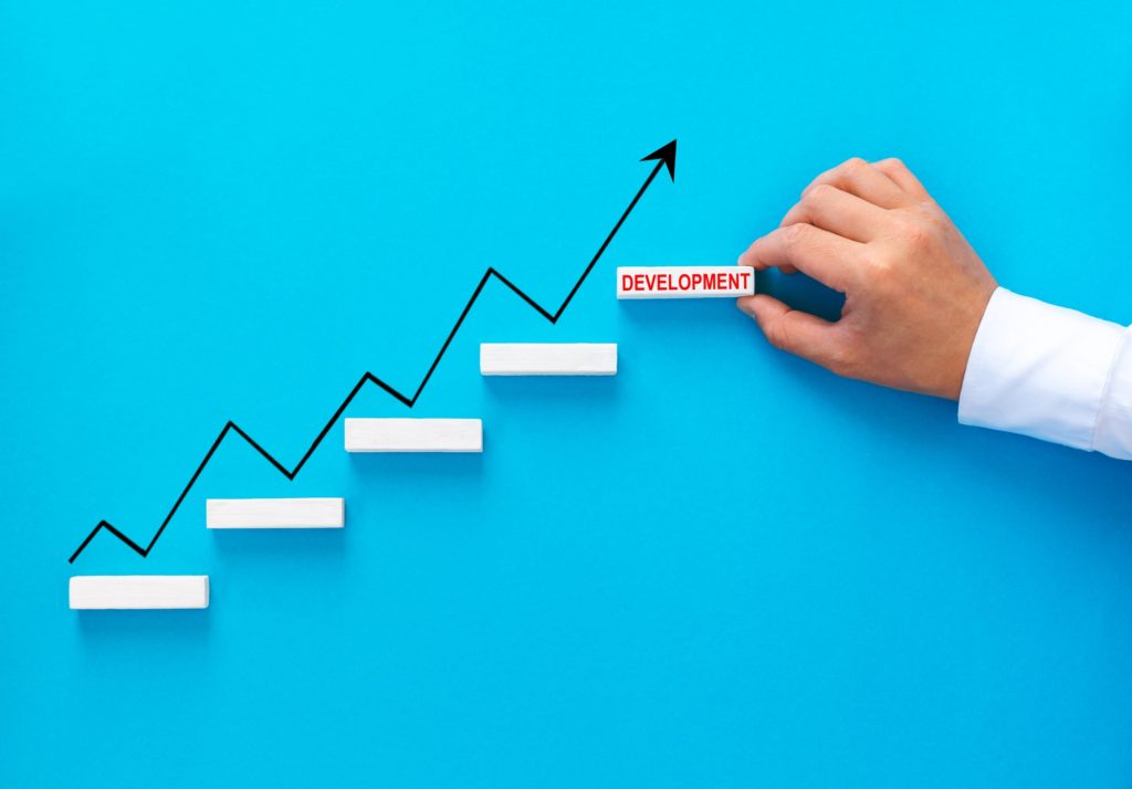 Businessman hand arranging wood block stacking as step stair with growth arrow. Business growth succ